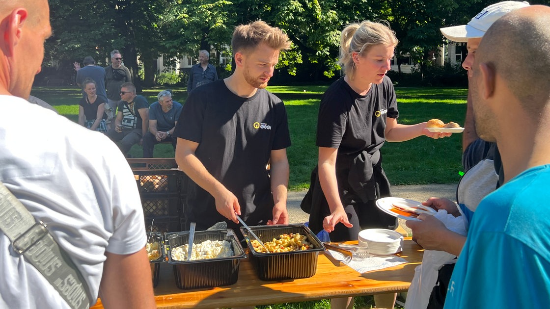 Ein Mann und eine Frau stehen hinter einem Biertisch und verteilen Essen an Menschen